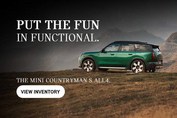 Green MINI Countryman S ALL4 parked on a grassy mountain overlook with rugged peaks in the background. Promotional text reads